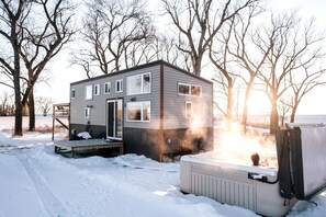 A small, two-story cabin with a deck, surrounded by snow and trees. - Gorgeous Tiny House, Peaceful Hills, Amazing Views (Ponca)