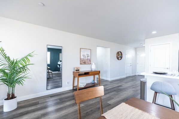 A modern kitchen with white cabinets, a wooden dining table, and a potted plant.