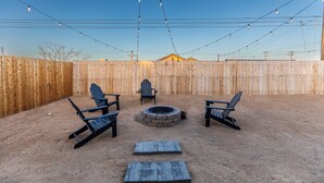 Un jardin avec une clôture en bois, un foyer et trois fauteuils Adirondack.