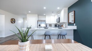 Une cuisine moderne avec des meubles blancs, un îlot central et un mur d’accent de couleur bleu-vert foncé.