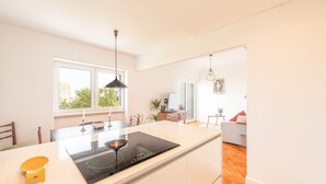 A modern kitchen with a central island, a dining area with chairs, and a view of the outdoors through large windows. - GuestReady - Spacious Flat in the heart of Lisbon (Lisbon)