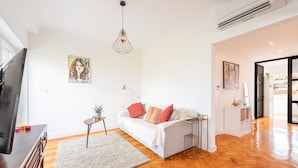 A modern living room with a white sofa, a small side table, a floor lamp, and a hanging light fixture. - GuestReady - Spacious Flat in the heart of Lisbon (Lisbon)