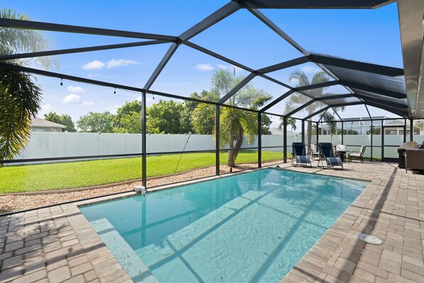 A covered swimming pool with lounge chairs and a view of a grassy yard.