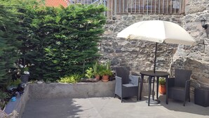 A stone wall with a green door, outdoor seating with a table and chairs, and potted plants. - Recanto das Florenças (3) – Stone House (Arco da Calheta)