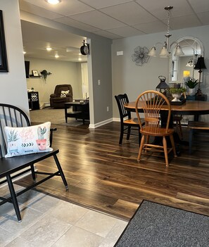 A dining area with a wooden table and chairs, a black chair with a cactus-themed pillow, and a grey rug. - Jemma’s Hideaway in Amish Country (Dundee)
