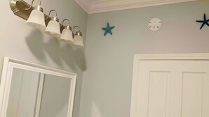 Un baño con puerta blanca, espejo, aplique de pared y decoración con forma de estrella.