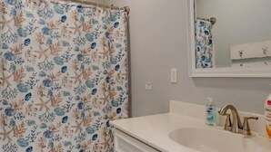 Un baño con cortina de ducha con motivos marinos, un lavamanos blanco con espejo y un inodoro.