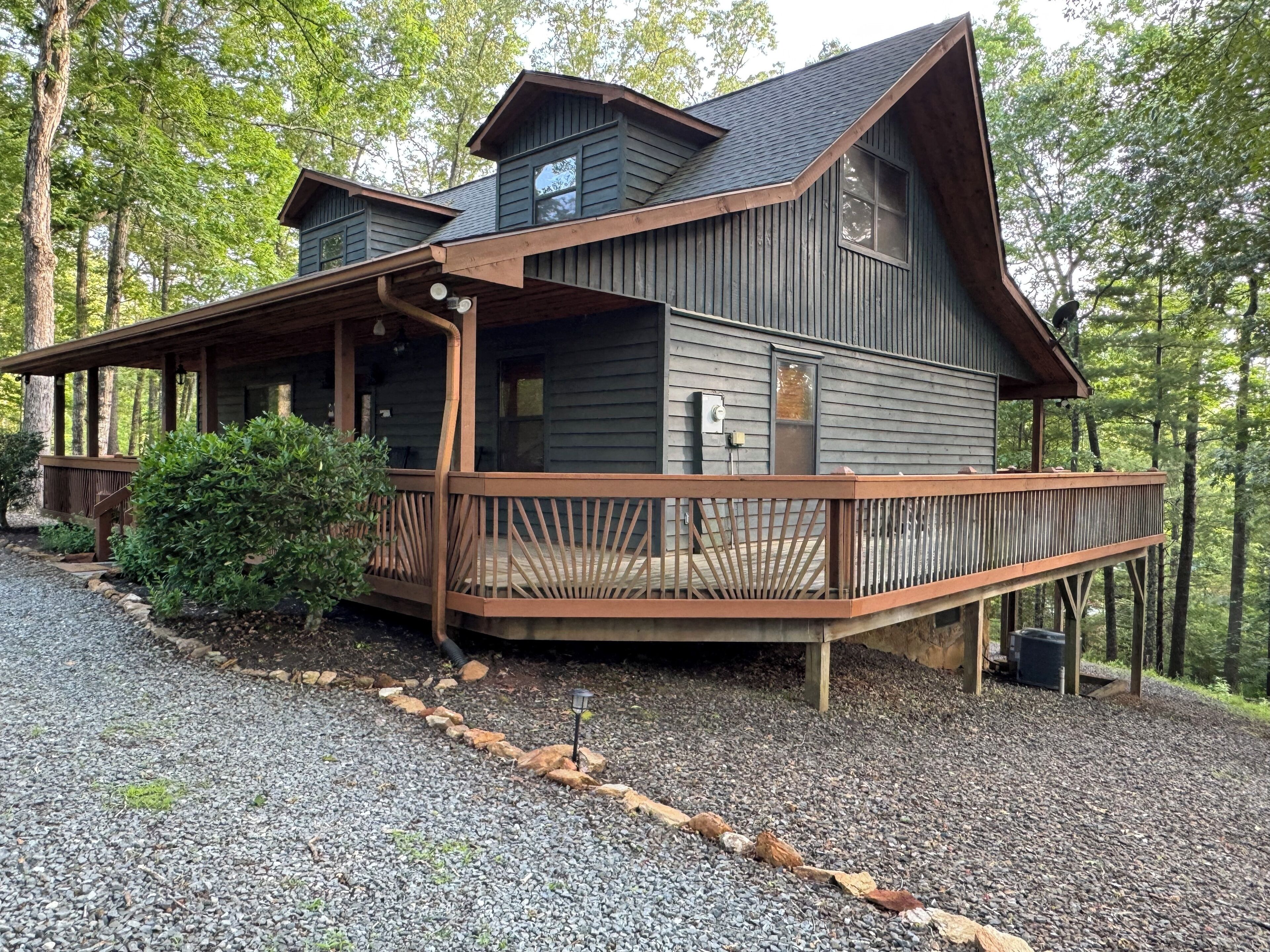 Une cabane à deux étages avec une terrasse en bois, entourée d’arbres.
