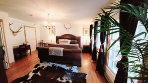 Une chambre à coucher avec un grand lit, un plancher en bois, un tapis en peau de vache, un lustre et des bois de cerf fixés au mur.