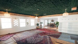 Une pièce spacieuse avec de grandes fenêtres, un plafond vert et plusieurs tapis sur le sol.