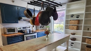 Une cuisine avec des armoires bleues, un plan de travail en bois, des casseroles suspendues, un four grille-pain et une fenêtre donnant sur un paysage verdoyant.