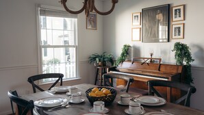 Une salle à manger avec un piano, une table à manger dressée avec des assiettes et des tasses, et des tableaux encadrés accrochés au mur.