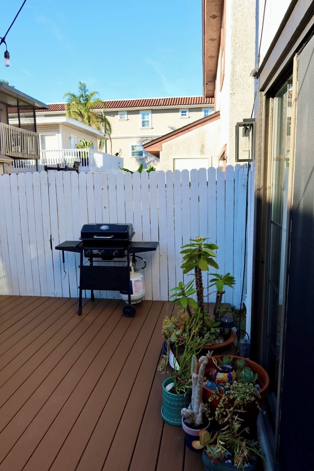 A wooden deck with a barbecue grill, potted plants, and a white picket fence.