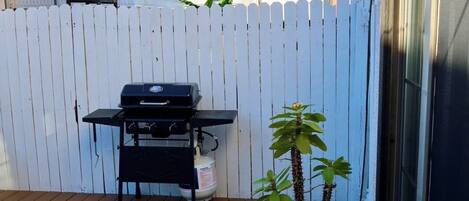 A wooden deck with a barbecue grill, potted plants, and a white picket fence.