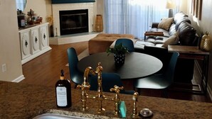 Un salon moderne avec une cheminée, une table à manger ronde et un coin cuisine équipé d’un évier et de robinets décoratifs.