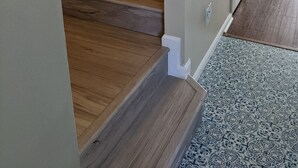 Un escalier en bois menant à un palier où se trouve un tapis à motifs.