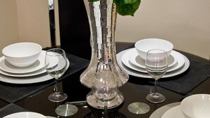 A dining table set with white plates, bowls, and wine glasses, centered by a silver vase with white flowers. - Lovely 2-bed Apartment in Stanford-le-hope (Stanford-le-Hope)