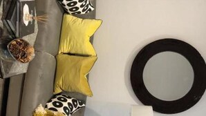 A modern living room with a grey sofa, yellow and black patterned cushions, a round mirror, and a small table with a bowl of fruit. - Lovely 2-bed Apartment in Stanford-le-hope (Stanford-le-Hope)