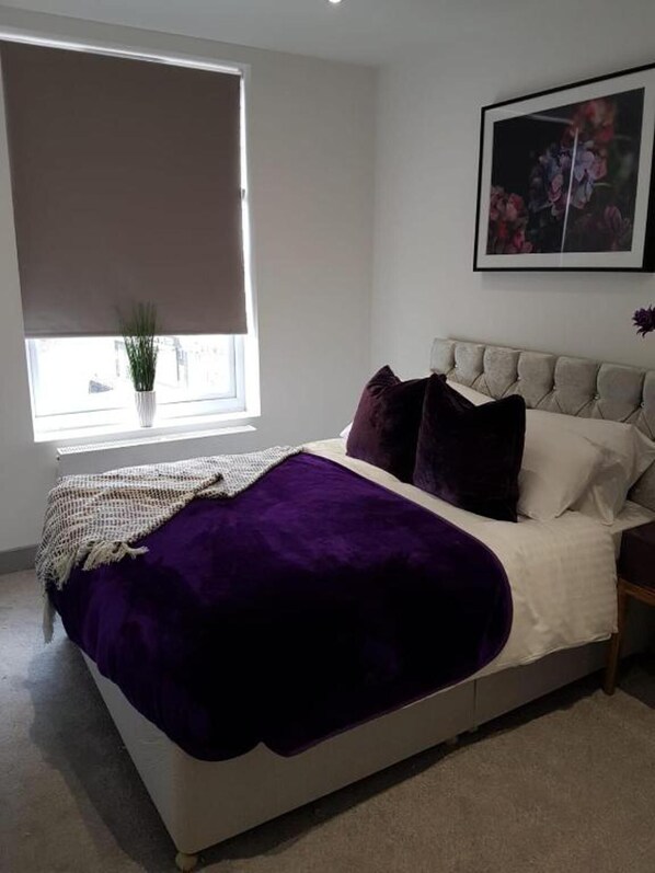 A bedroom with a bed, a window with a plant, and a framed picture on the wall.