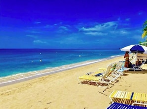 A beach with clear blue water, sun loungers, and umbrellas. - Beach Apartment, Walk to the Beach! (Rincon)