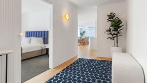 Une chambre d’hôtel avec un lit, un bureau et une chaise. Il y a une plante dans un coin et une fenêtre avec des rideaux.