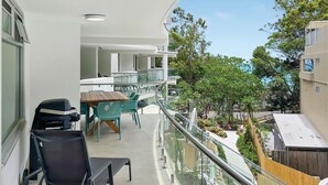 Un balcon avec une table et des chaises, un barbecue et une vue sur les bâtiments et la verdure environnants.