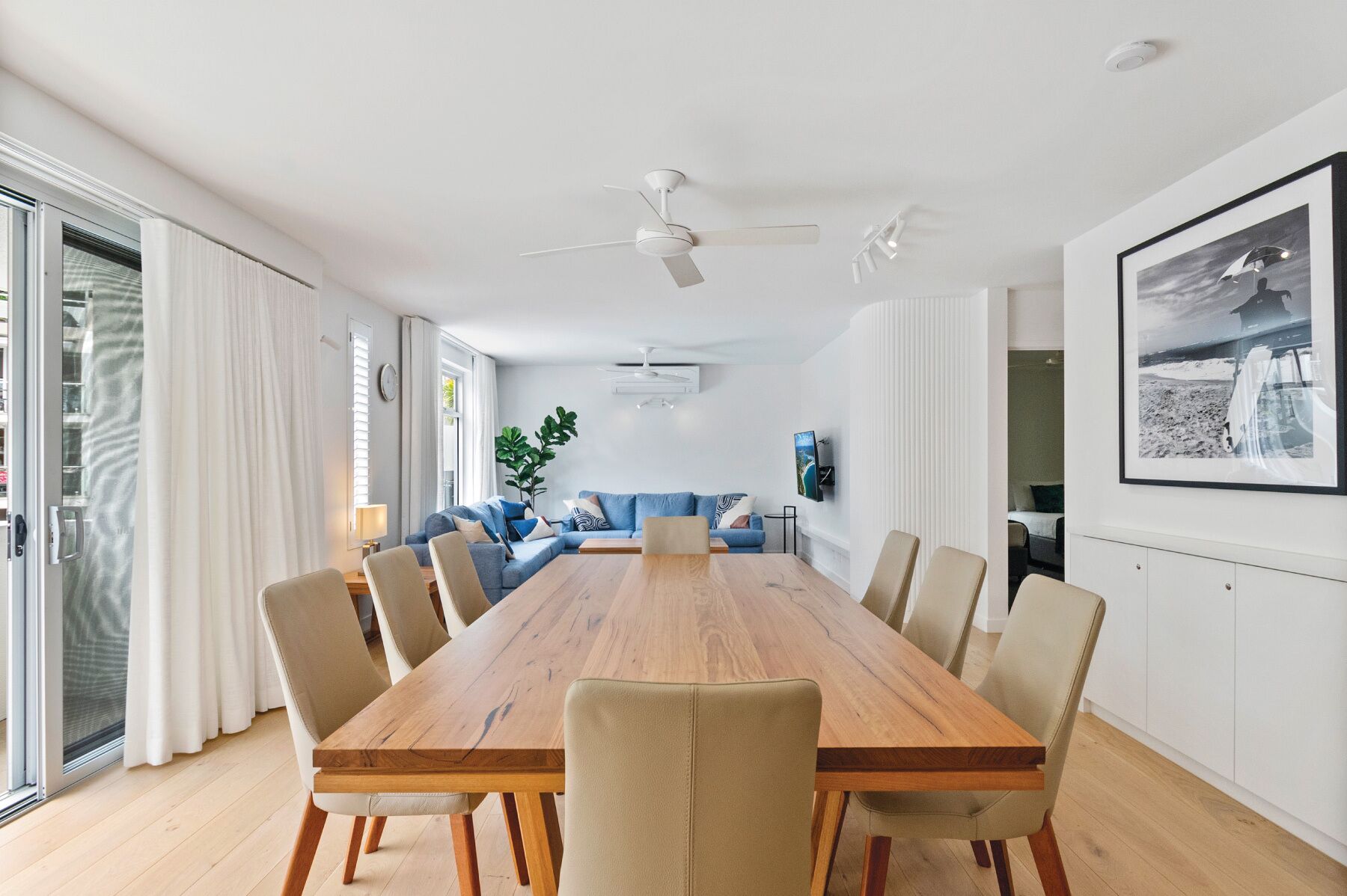 Une salle à manger moderne avec une table et des chaises en bois, un canapé bleu et un ventilateur de plafond.