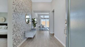 A modern interior with a patterned wallpaper, a grey sofa, and a dining area with natural light. - Specials-ask +gameroom+basketball+fire pit+bbq+beautiful pool+spa+mountain views (Desert Hot Springs)