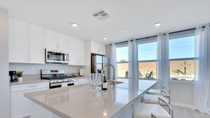 A modern kitchen with white cabinetry, stainless steel appliances, and a large island with bar stools. - Specials-ask +gameroom+basketball+fire pit+bbq+beautiful pool+spa+mountain views (Desert Hot Springs)