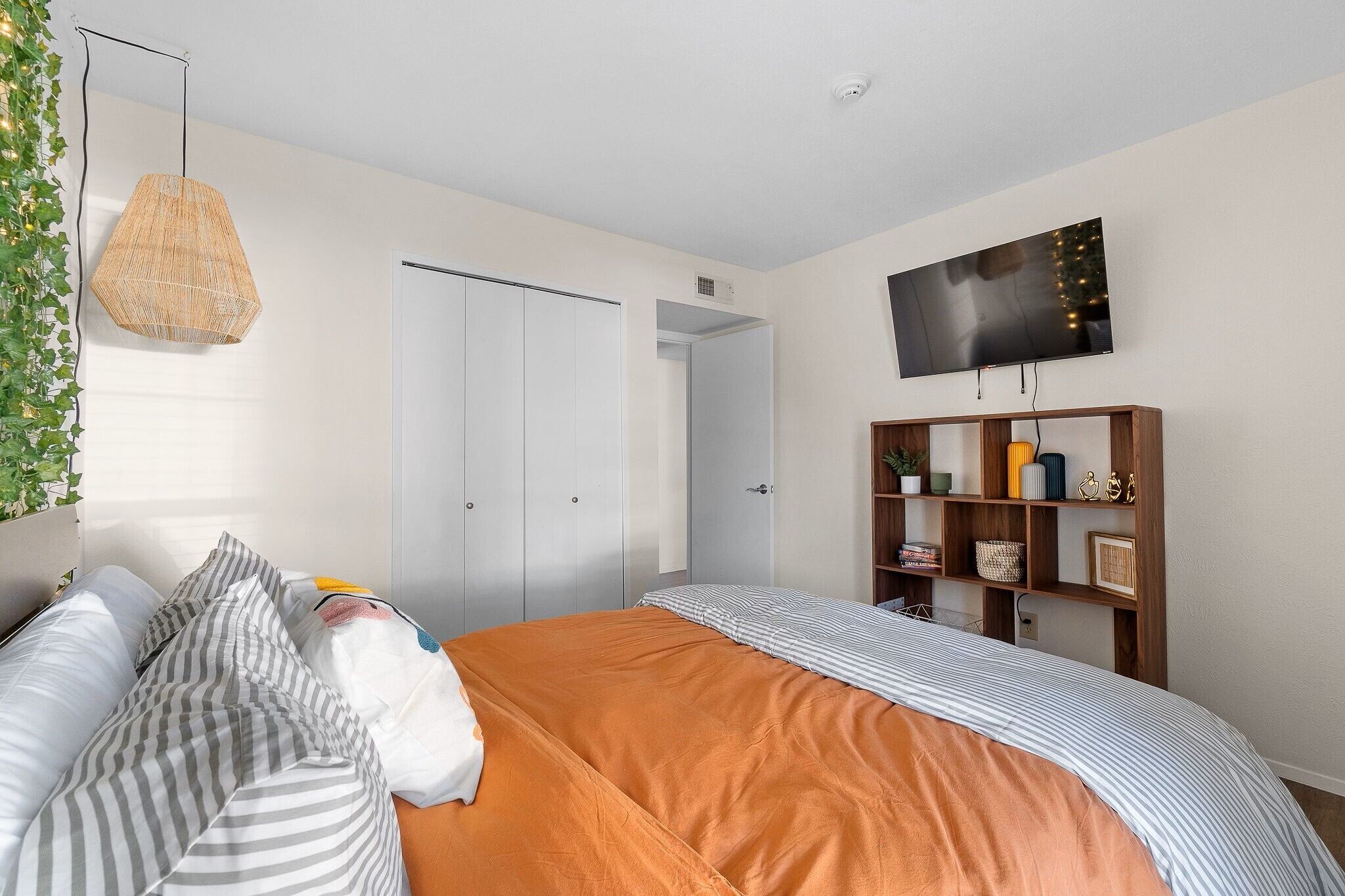 A bedroom with a bed, a hanging light fixture, a television on the wall, and a wardrobe.