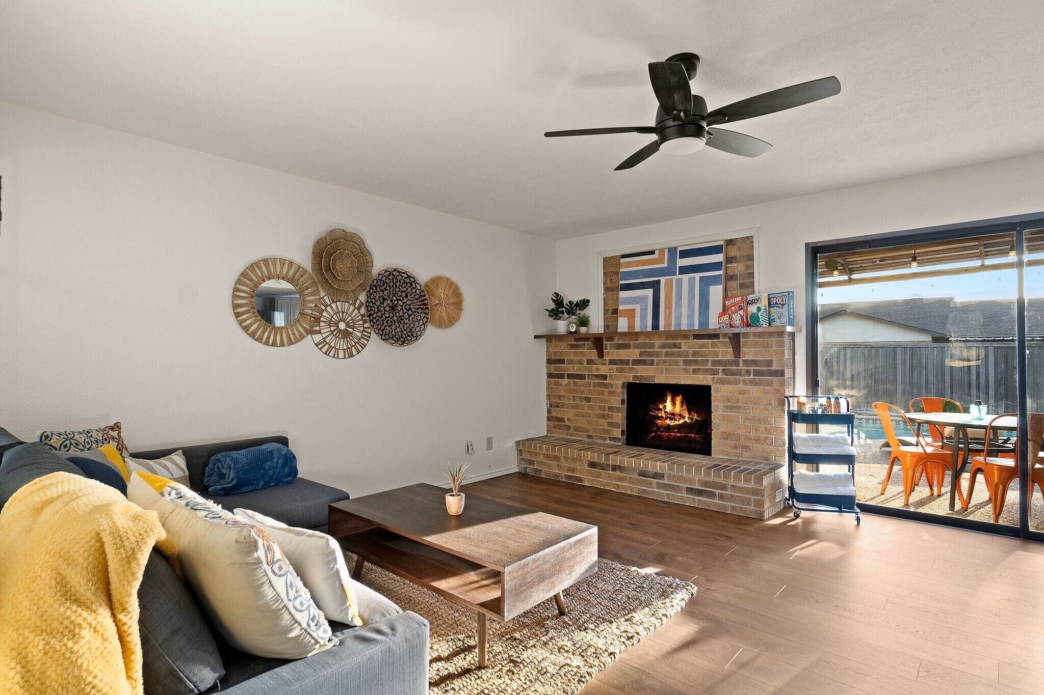 Ein modernes Wohnzimmer mit Kamin, Deckenventilator und Blick ins Freie.