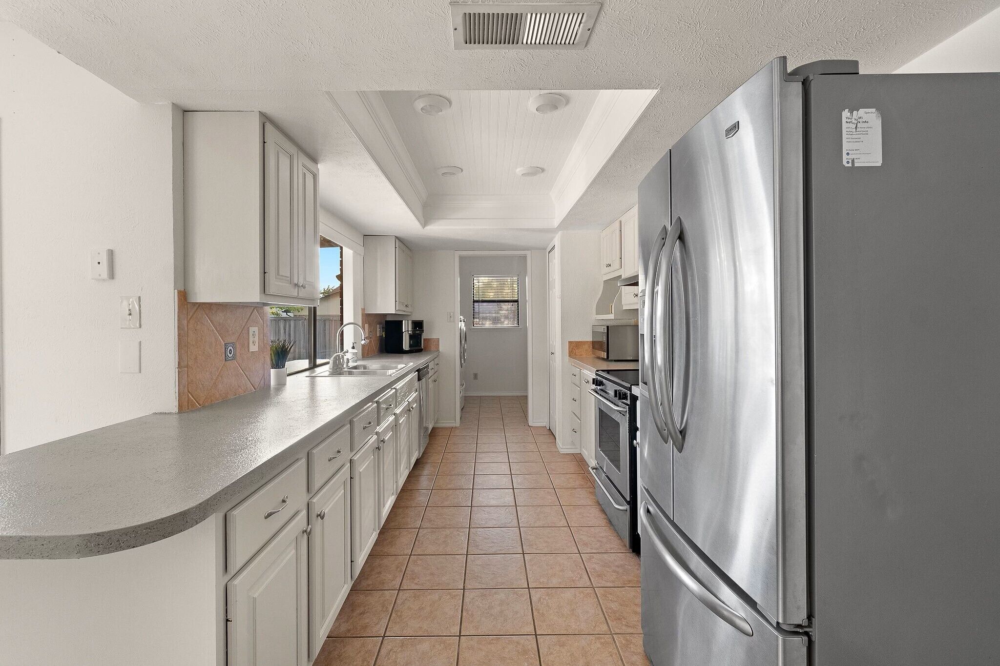 Una cocina con armarios blancos, un refrigerador de acero inoxidable y piso de baldosas.