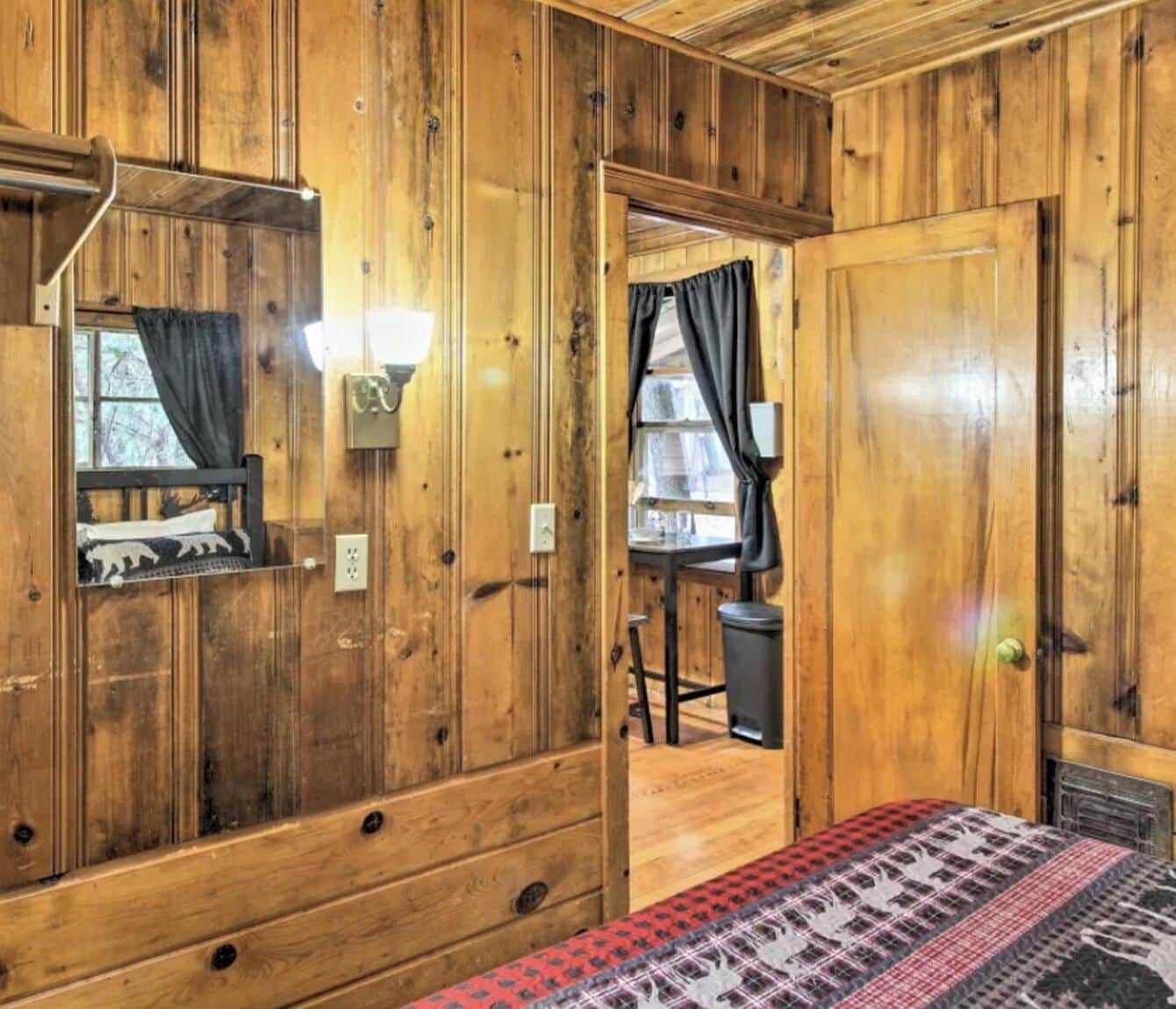 A wooden room with a bed, a desk, and a window with curtains.