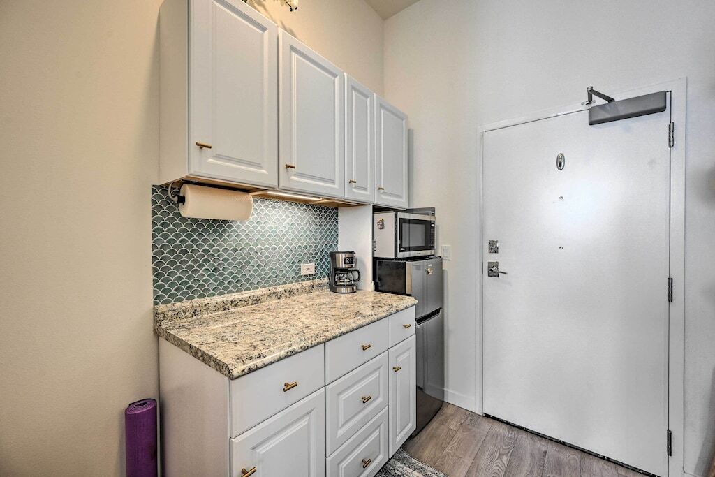 A compact kitchen with white cabinets, a granite countertop, a microwave, and a coffee maker.