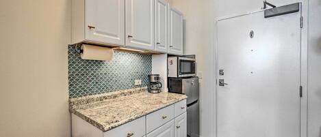 A compact kitchen with white cabinets, a granite countertop, a microwave, and a coffee maker.