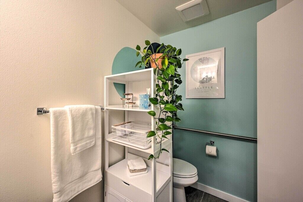 A bathroom with a white vanity, a hanging plant, a toilet, and a framed picture on the wall.