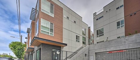 Ein modernes, mehrgeschossiges Gebäude mit einer Fassade aus Holz und Beton, einem verschlossenen Eingang und einem überdachten Parkplatz.