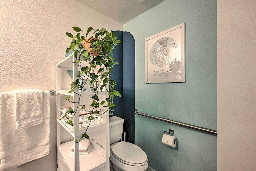 Une salle de bain avec des toilettes blanches, un porte-serviettes, une carte encadrée de Seattle et une plante dans un meuble de rangement blanc.