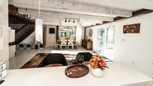 Un vaste espace de vie comprenant une table à manger, des fauteuils en cuir noir et une table basse en bois agrémentée de verres à vin et d’un vase de fleurs.