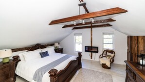 Une chambre avec un grand lit, des poutres en bois, une télévision, une chaise et une commode.