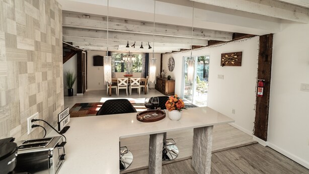 Une cuisine moderne dotée d’un grand îlot central, d’un coin repas avec une table et des chaises en bois, et offrant une vue sur l’extérieur.