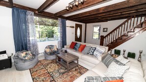 Un salon avec un canapé blanc, un fauteuil poire gris, une table basse en bois et un tapis à motifs.