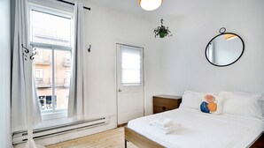 A bedroom with a wooden bed, white bedding, a round mirror, and a potted plant. - La Maison Du Mile-End (Montreal)