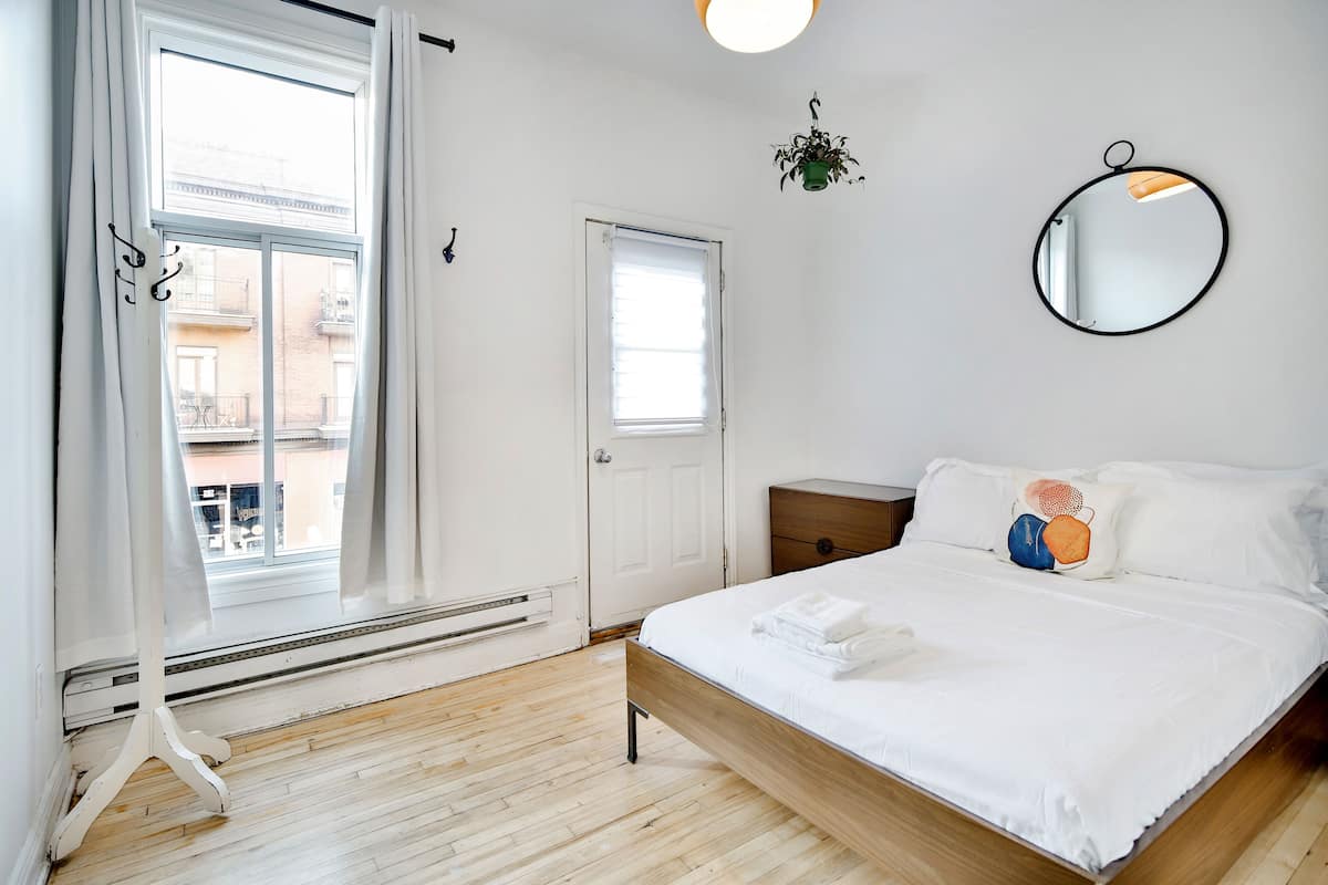 A bedroom with a wooden bed, white bedding, a round mirror, and a potted plant.