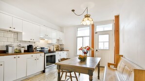 A kitchen with white cabinets, a wooden table, and a bench. - La Maison Du Mile-End (Montreal)
