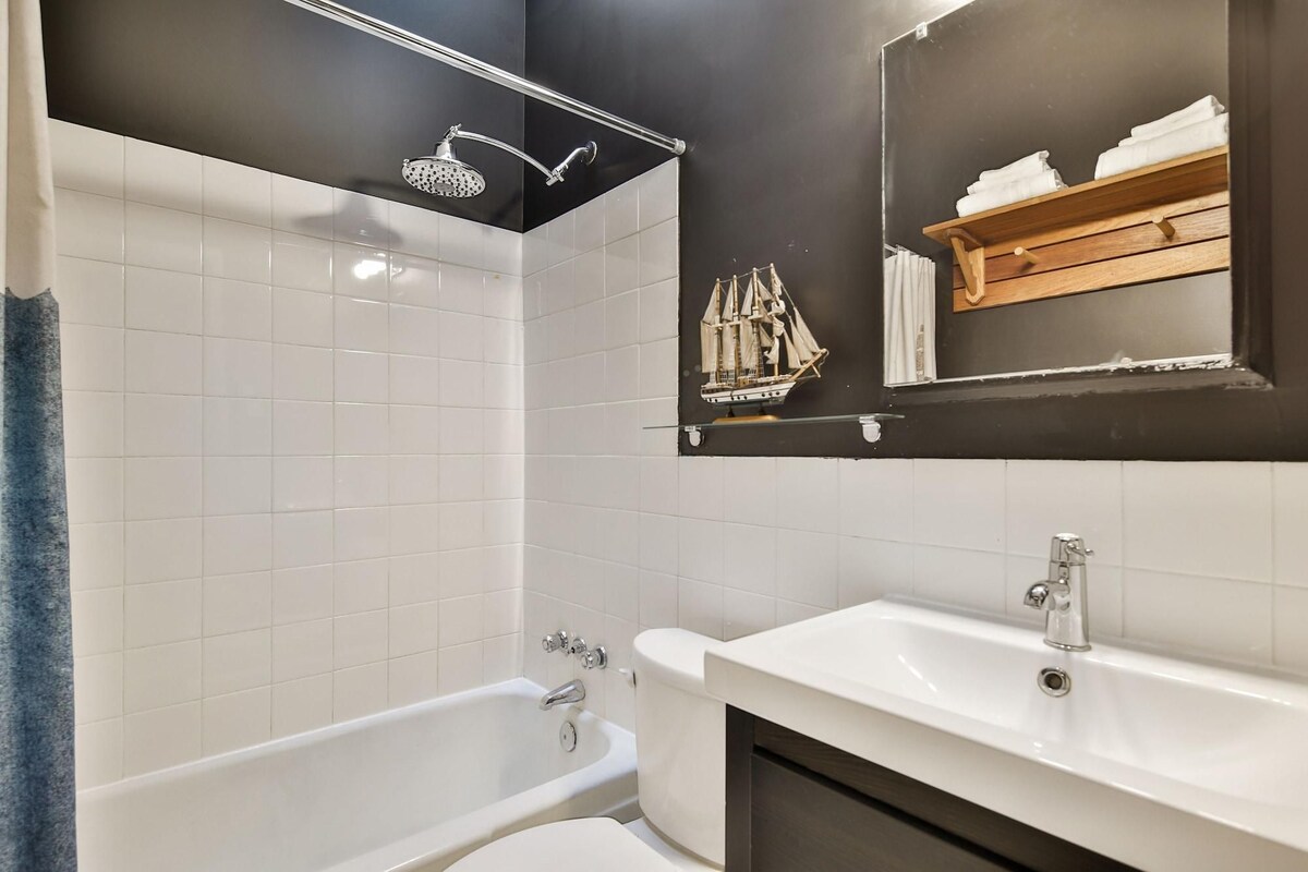A modern bathroom with a bathtub, a shower, and a sink. There is a ship model on the wall and a towel rack with towels.