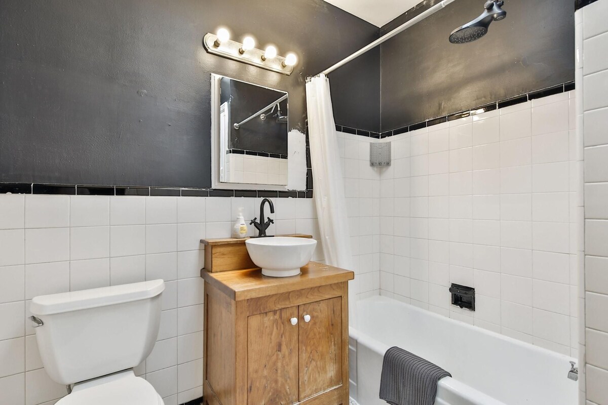 A bathroom with a white toilet, a wooden vanity with a white sink, a mirror, and a shower area.