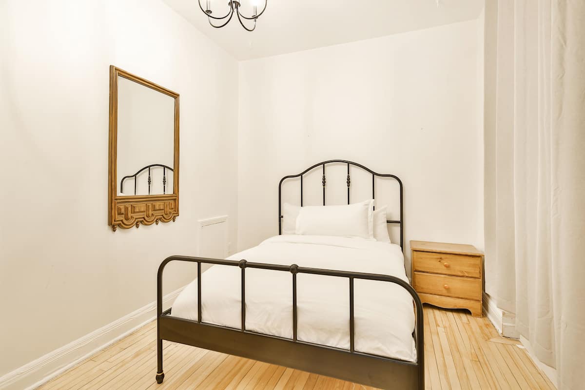 A bedroom with a metal-framed bed, a wooden nightstand, a mirror, and a white wall.
