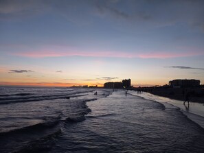 A beach at sunset with waves, buildings, and people. - Heart of the Sandy beach, 1 bed 1 bath apartment (Puerto Peñasco)
