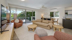 A modern living room with a sofa, two round tables, a ceiling fan, and a kitchen area with a counter and cabinets.